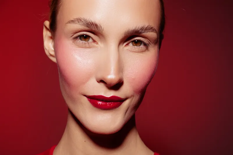 Close-up portrait of a woman with glossy red lipstick and natural skin on red background. Concept of beauty, makeup, skincare, and confident female model with smooth complexion.