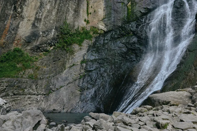 waterfall cascade flowing down rugged rocky cliff with green moss and vegetation surrounding the natural landscape in misty forest atmosphere