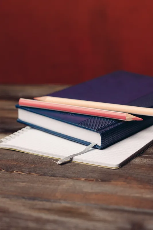 На деревянном столе лежат книги, блокноты и ручки, создавая рабочую атмосферу