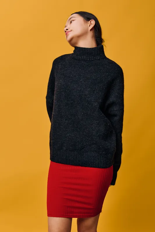 Young woman in black sweater and red skirt posing with head turned on yellow background. Casual outfit, fashion style, confident model with neat hairstyle and relaxed posture.