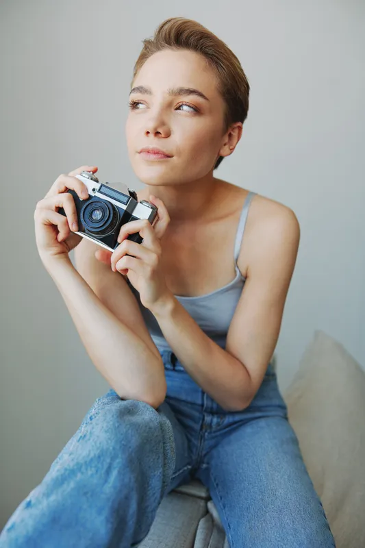 Женщина-фотограф снимает в студии на старую плёночную камеру, сидя на диване дома
