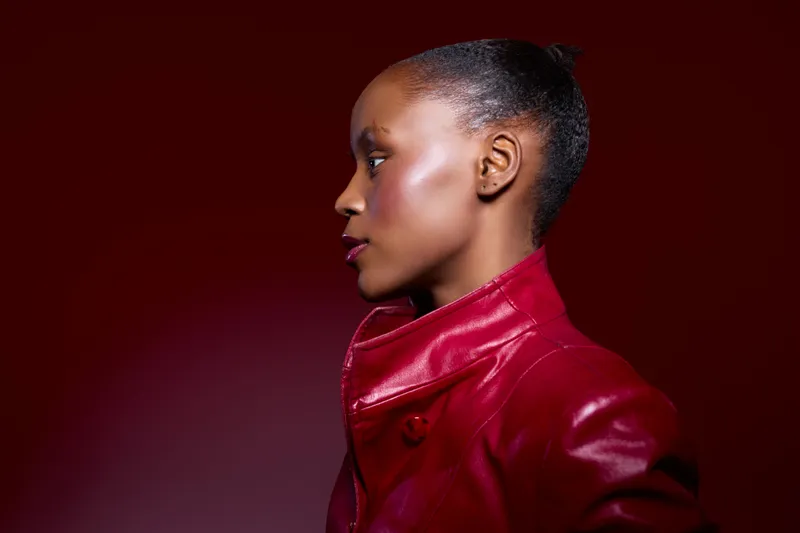Profile of a dark skinned African woman wearing a red leather jacket on a dark red background. Concept for fashion, style, elegance, and beauty with studio lighting.