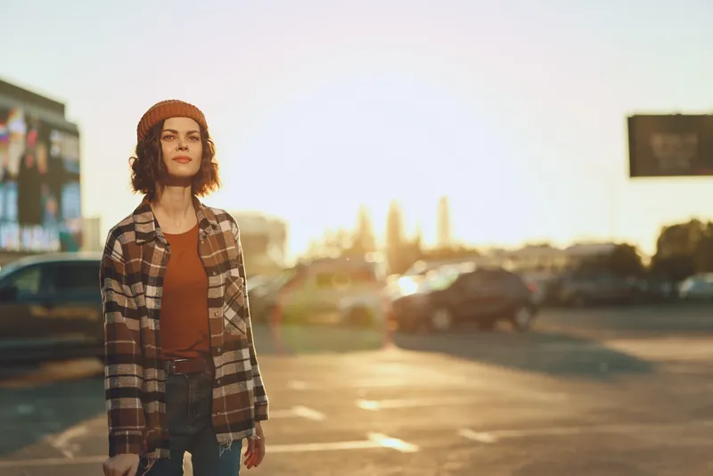 Woman portrait in an urban parking lot at golden hour, candid beanie look with sunlight and glow, authenticity and mindful living captured in emotional storytelling and relaxed lifestyle.