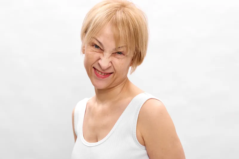 elderly woman portrait with blonde hair smiling softly in a studio on a white background casual white tank top senior retirement concept gentle age