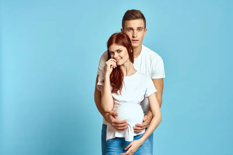 Беременная женщина в белой футболке и мужчина, супружеская пара, ожидающая ребенка, на голубом фоне