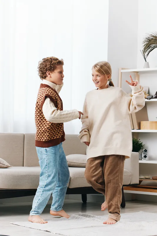 Two children dance together in a bright living room, barefoot and smiling, capturing a moment of pure joy and playful energy as they share a friendly routine.