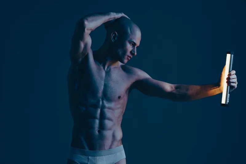 Athletic man demonstrating strength and confidence holding a light source, captured in a studio setting with a moody atmosphere. Perfect for fitness themes.