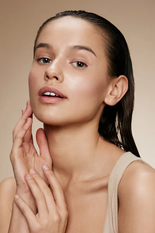 A portrait of a young woman with fresh, dewy skin and wet hair, conveying natural beauty and self care through soft lighting and a neutral background