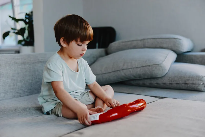Young boy focused on playing a toy instrument indoors, surrounded by cozy furniture and soft lighting, showcasing creativity and playfulness.