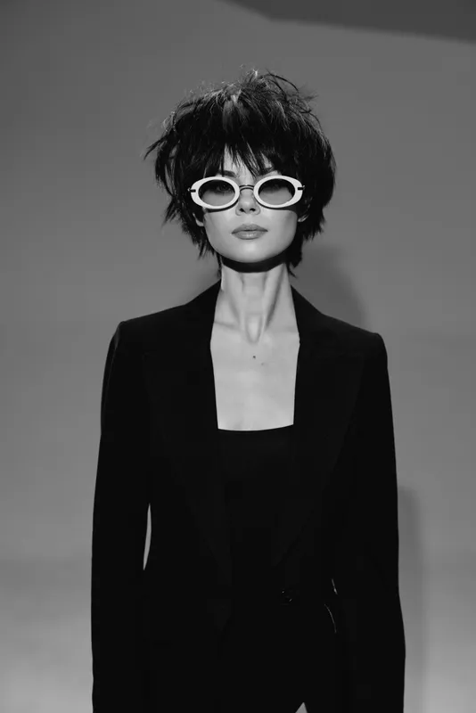 Black and white portrait of stylish woman wearing sunglasses and black outfit with short hair in studio setting
