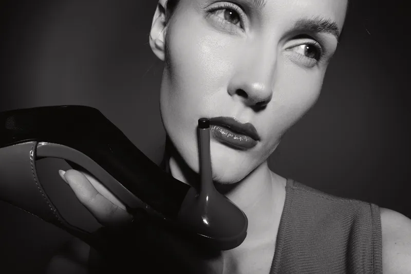 Closeup of white woman holding high heel shoe near lips in black and white photo. Concept of fashion, elegance, and vintage style.