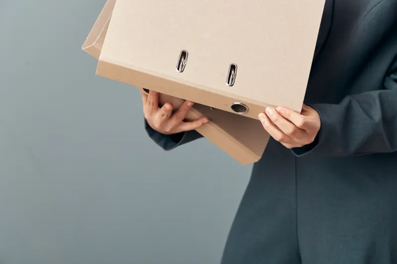 Person in suit holding cardboard folders with documents for office organization and paperwork. Business, file storage, professional workspace with hands carrying files for work tasks.