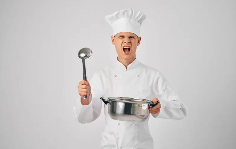 Шеф-повар с профессиональной кухонной утварью занимается приготовлением еды, ресторанное обслуживание