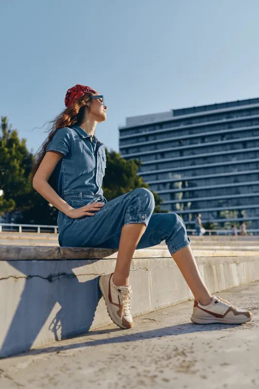 lifestyle woman wearing modern boho-western denim street style outfit with casual sneakers and red hat, captured in warm film color outdoor setting