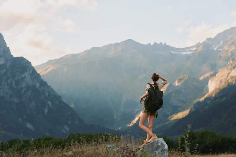 Young woman hiking in a rugged mountain landscape, wearing a backpack, standing on a rock and savoring panoramic scenery, a lively outdoor lifestyle moment in nature