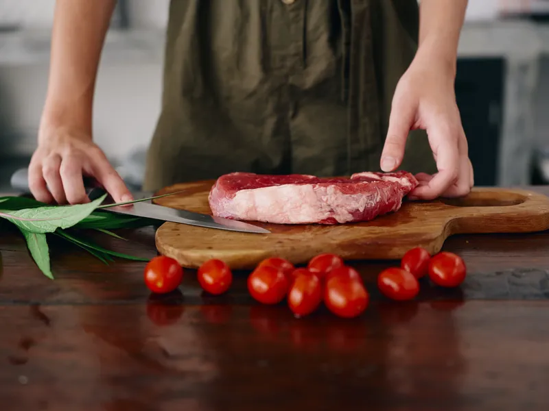 Женщина с ножом в руке нарезает свежее стейковое мясо для жарки на кухне