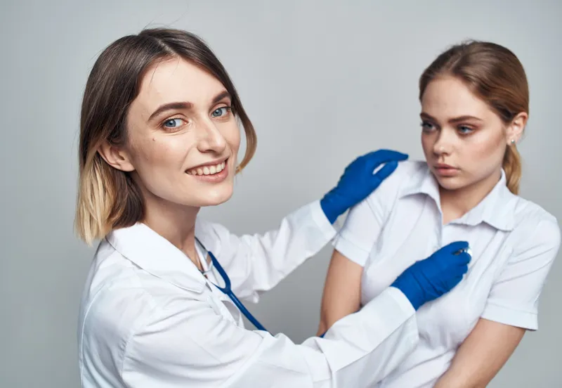 Счастливая женщина-врач в синих перчатках и пациентка в белой футболке