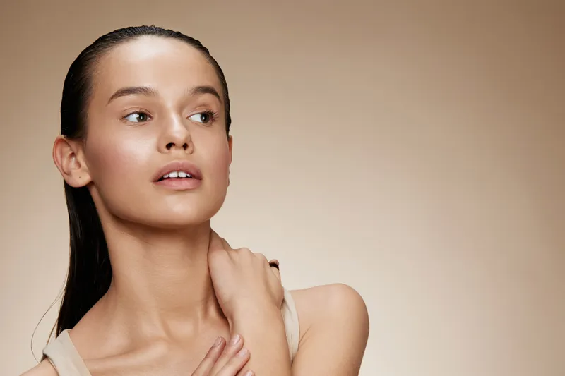 Portrait of a young woman with a natural look and soft makeup, showcasing healthy skin and a serene expression against a neutral backdrop