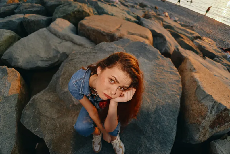 lifestyle woman in modern boho-western denim street style sits on rocks with thoughtful expression, natural light and film color enhancing vintage vibe