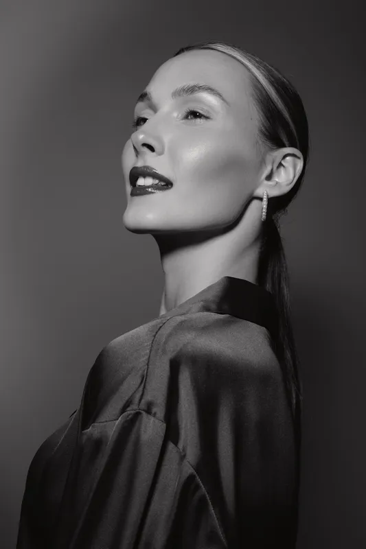Close-up portrait of a fair skinned Caucasian woman with slicked back hair and glossy lips in black and white studio lighting.