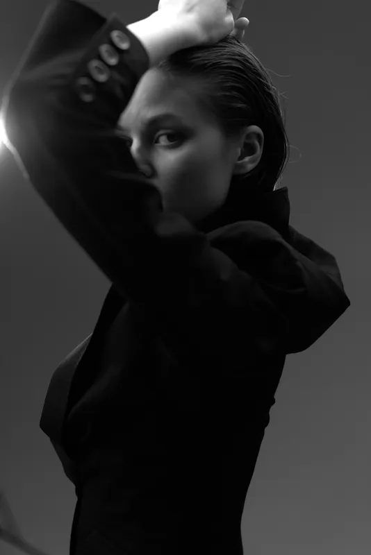 Black and white portrait of a confident woman in a dark blazer with wet hair, posing stylishly in a studio setting.