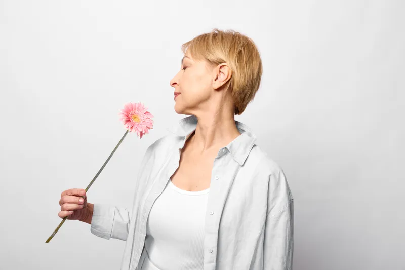 Woman blonde profile holding flower pink dandelion portrait spring mood, soft light studio shot, calm smile in casual shirt, white background, style