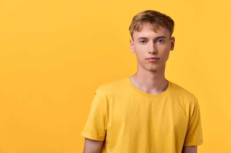 Yellow clad man standing against a bright yellow backdrop wearing a plain t shirt, minimal studio styling, contemporary fashion vibe, soft lighting emphasizing color harmony and calm, clean