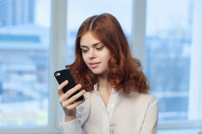 Симпатичная женщина в рубашке с телефоном в руке