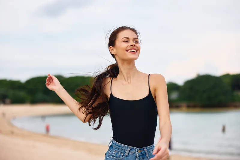 Женщина улыбается на пляже, чувствуя себя беззаботной и молодой