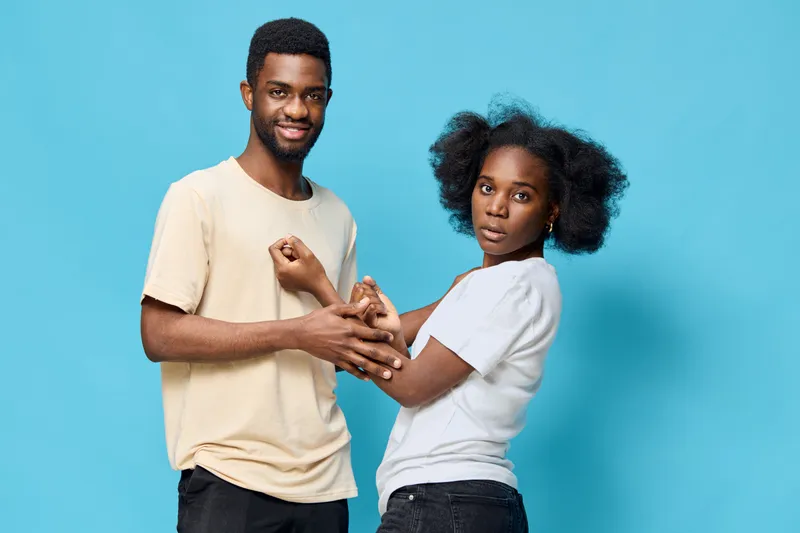 Young African couple expressing joy and connection against a bright blue background, wearing casual clothing, showcasing emotions of love and togetherness