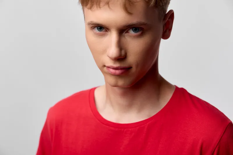 Young man in a red shirt, close up in a studio with a neutral background and soft lighting, focused expression, clean casual style suitable for fashion, lifestyle and editorial photography