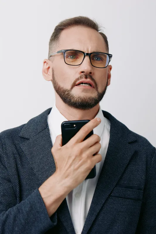 A professional man in a blazer and glasses holds a smartphone, displaying thoughtful concern against an isolated colorful background, suited for business and leadership contexts.