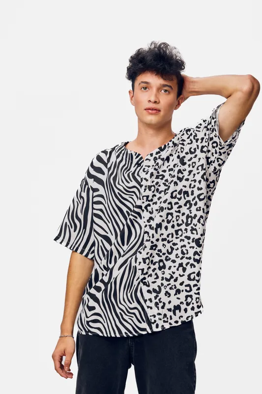 young man in animal print t-shirt posing with hand on head against white background, curly hair, casual style, trendy fashion, neutral expression