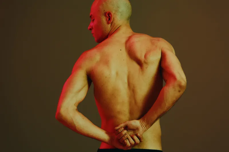 Fit man with muscular back and strong arms poses against a gradient background, showcasing body fitness in a vibrant light concept.