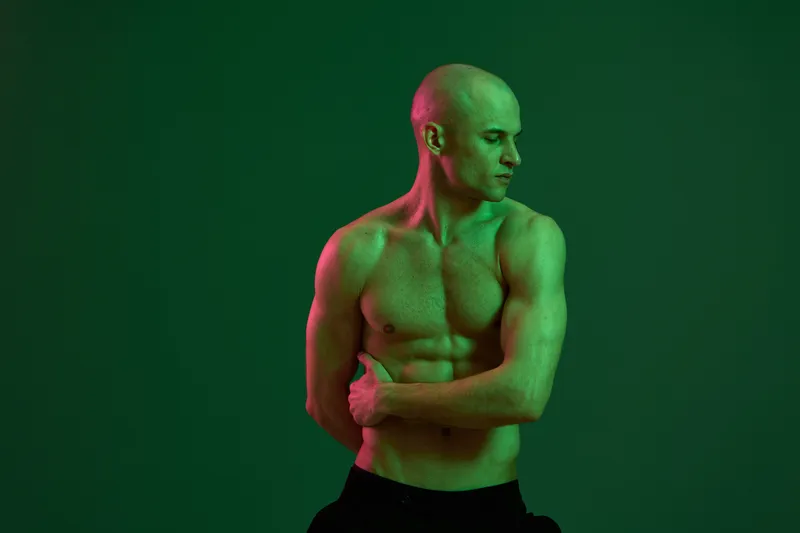 Athletic man with a muscular build poses confidently in a dramatic green lighting setup, showcasing strength and determination in a striking visual display.