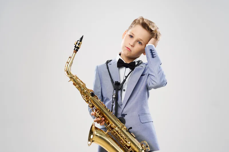 Юный музыкант в костюме исполняет композицию на саксофоне