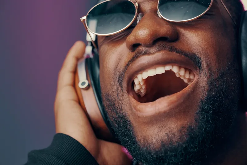 Happy young Black man singing passionately with headphones on, showcasing joy and energy in a vibrant atmosphere
