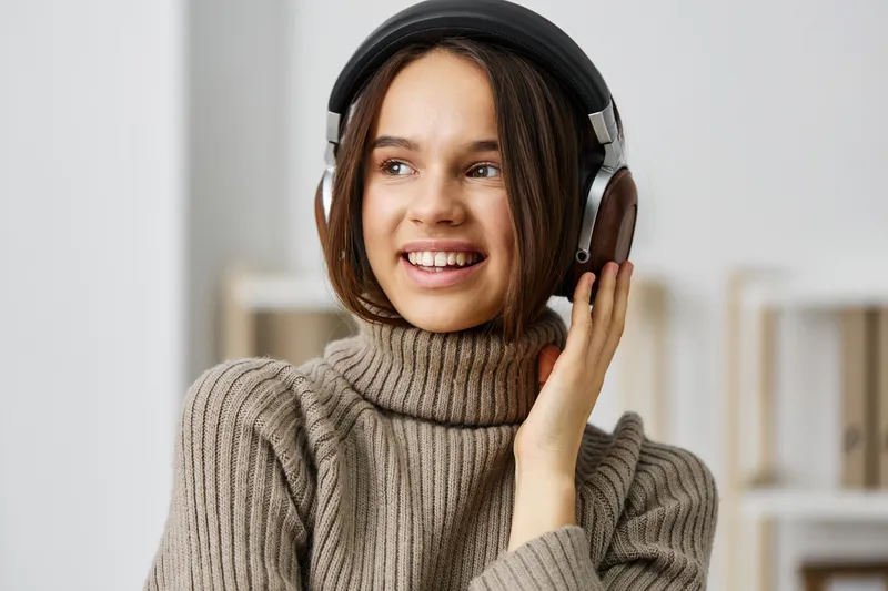 Молодая женщина в наушниках слушает музыку на смартфоне, сидя дома