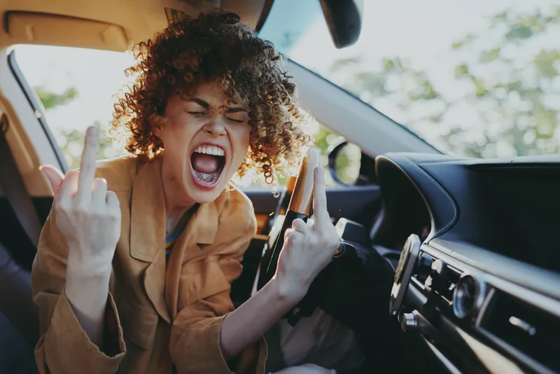 Energetic woman inside a car, shouting playfully, bold expression, sunlit interior, retro film color mood, candid lifestyle moment, vibrant and rebellious