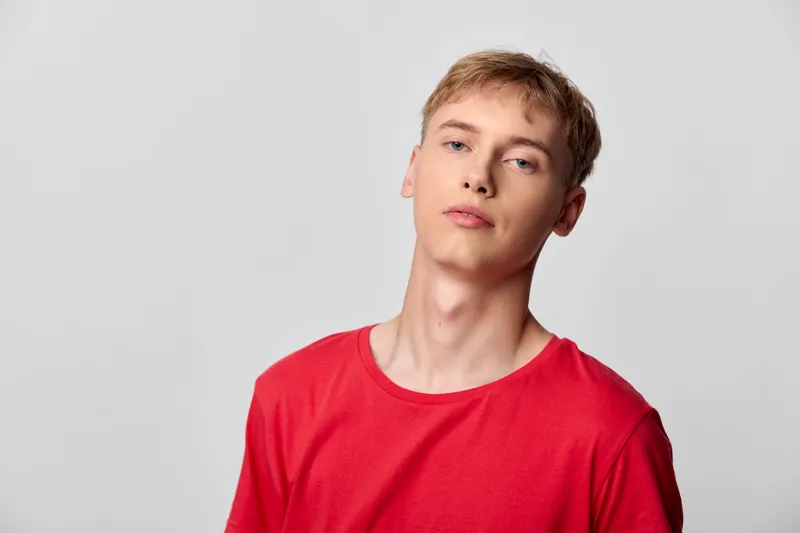 Young man in a red t shirt stands against a plain gray background, casual mood, relaxed expression, simple studio shot without branding or accessories