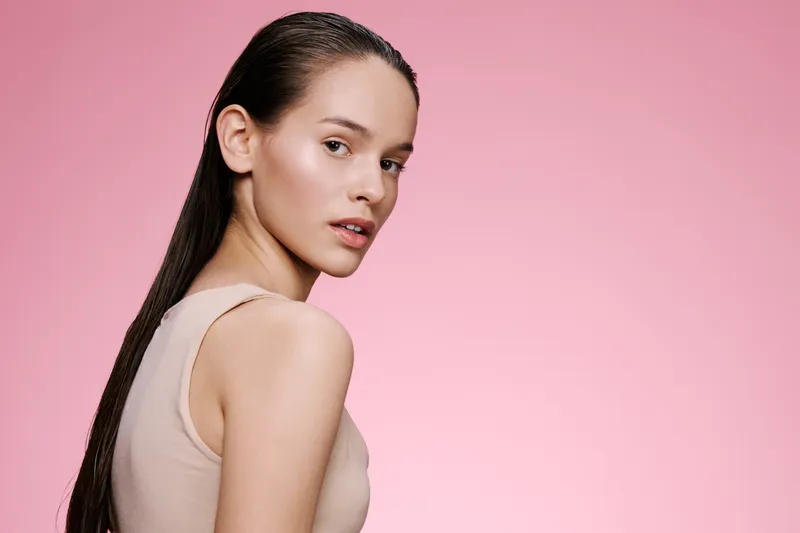 Elegant young woman with long hair on a pink background, showcasing natural beauty and confidence, representing modern femininity in a minimalist fashion style