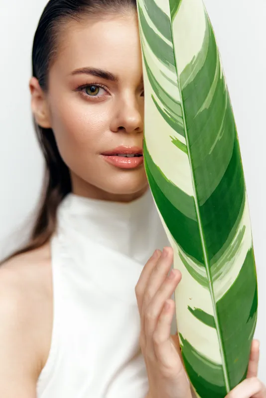 Молодая женщина прячет лицо за большим тропическим листом, демонстрируя безмятежное выражение