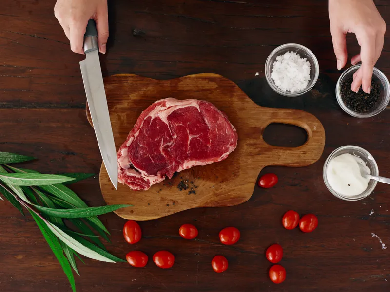 Женщина с ножом в руке нарезает свежее мясо стейка для жарки на кухне