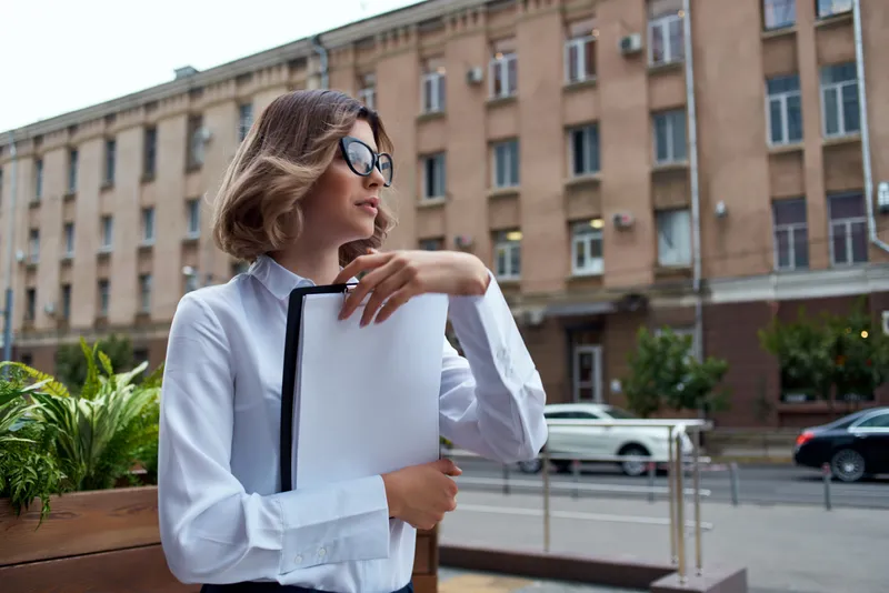 Женщина-менеджер в белой рубашке с документами на улице