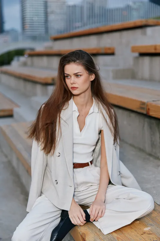 Confident woman in business attire seated outdoors, showcasing modern elegance and professionalism in a cityscape environment.
