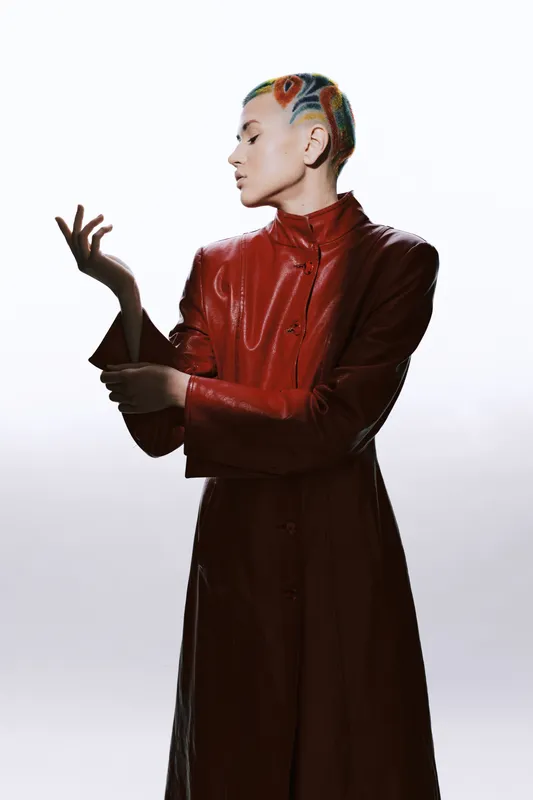 woman with colorful short hair wearing a red leather coat, graceful pose, minimalist white background, artistic and modern fashion style, stylish female portrait