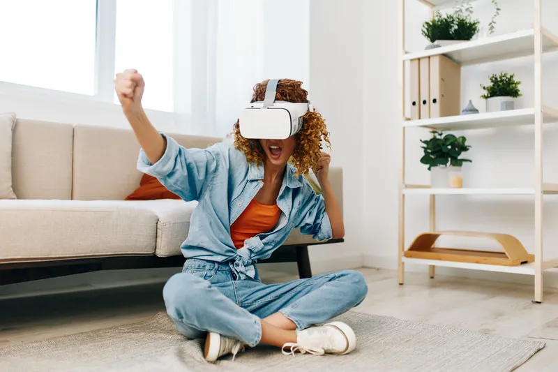 Блаженство виртуальной реальности: улыбающаяся женщина дома в VR-очках, наслаждающаяся футуристической игрой на диване