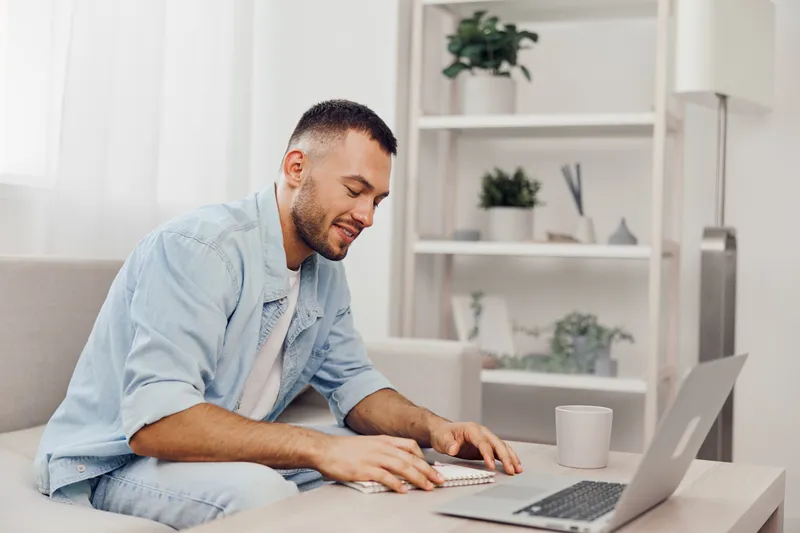 A focused man working on his laptop in a cozy living room, embracing a moment of digital detox while navigating work-life blur and personal growth.