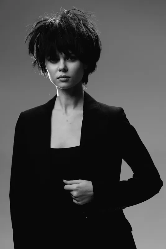 Black and white portrait of a stylish woman with short hair wearing a dark blazer and confident expression.