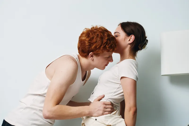 Couple, intimacy, affection, love and young redhead man whispering to woman in casual clothes with white background. Relationship, connection and romance with emotional gesture.